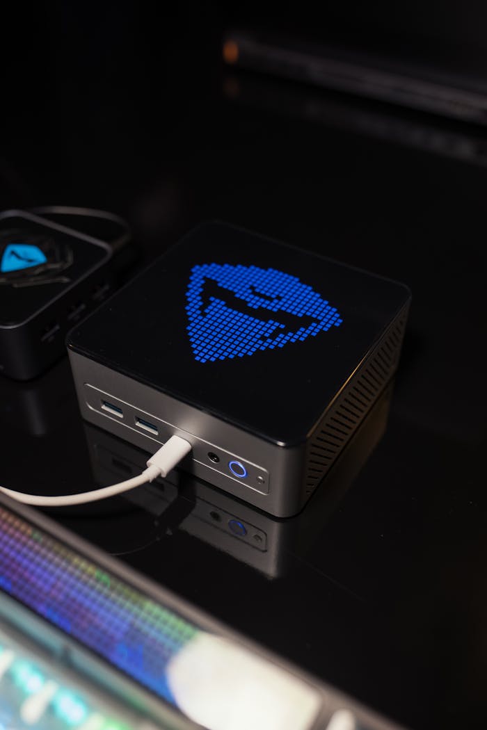 Compact mini PC with customizable digital display glowing in blue on a dark desk setup.